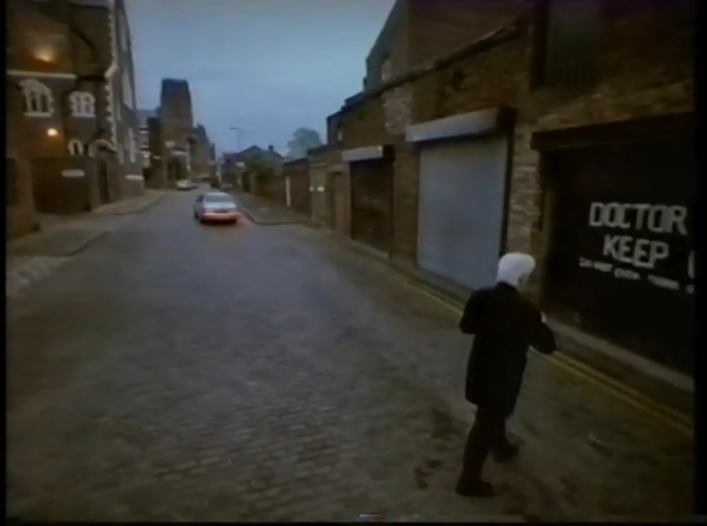 Figure wearing black coat with white hair walking to garage door