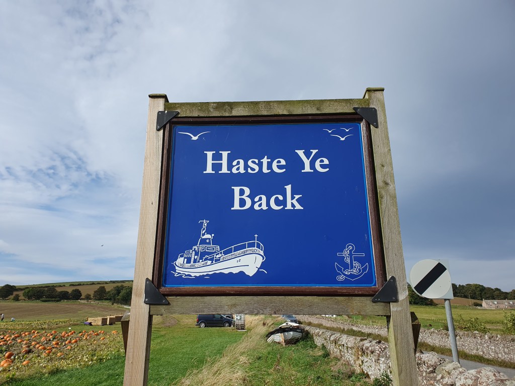 'Haste Ye Back' sign with a boat and anchor, by pumpkin field