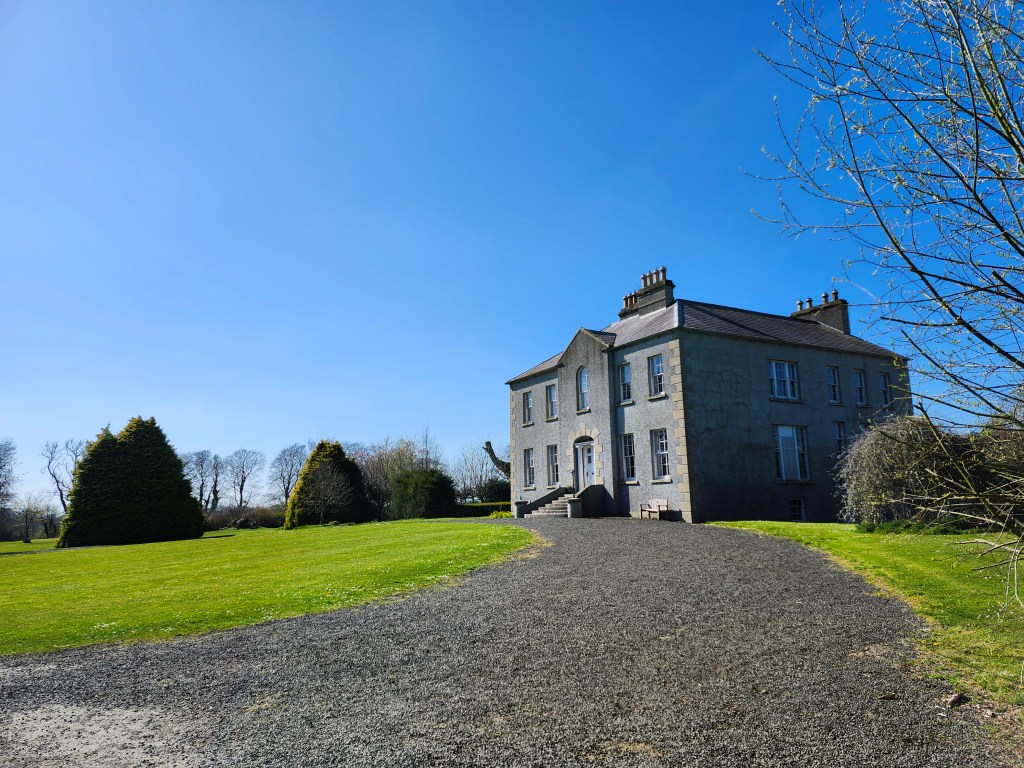 A large house in a garden with a long driveway up to it