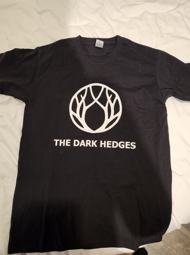 A black t shirt with a white logo and the text 'The Dark Hedges'
